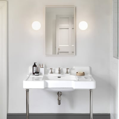 Et moderne badeværelsesinteriør med to Astro Zeppo væglamper flankerende et stort spejl over en hvid porcelænsvask.