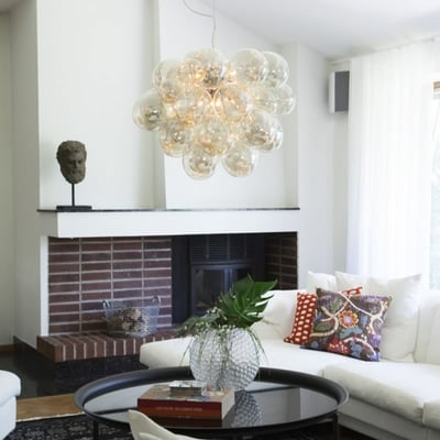 By Rydéns Gross Grande lysekrone monteret i en moderne stue med hvid sofa og en pejs, diameter 62 cm med ravglaskugler.