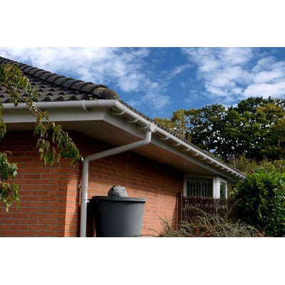 Plastmo tagrende monteret på en rød murstensbygning med grønne træer i baggrunden og en blå himmel.