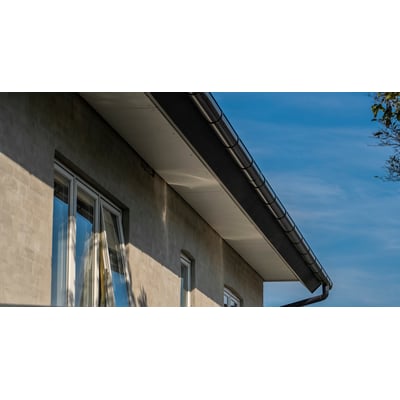 Plastmo sort tagrende monteret på en lys facade med hvide vinduer mod en klar blå himmel.