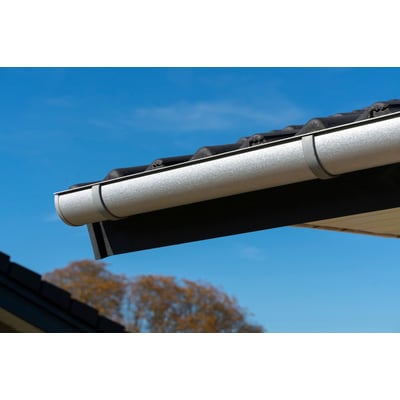 Plastmo tagrende i aluzink med en bredde på 120 mm, monteret på et mørkt hus med grå tagsten.