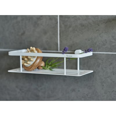 Smedbo Sideline brusekurv i mat hvid, 250x103 mm, med en træmassagebold og grønne planter på en grå flisevæg.