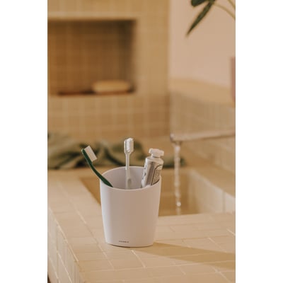 Cosmic Saku tandkrus i mat hvid med tandbørster og tandpasta sat i, placeret på en lys flisebelagt bordplade.