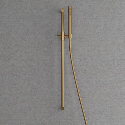 Detaljeret visning af Scandtap brusesætets stick-formede håndbruser og 1500 mm slange i børstet messing, monteret på en betonlignende baggrund.