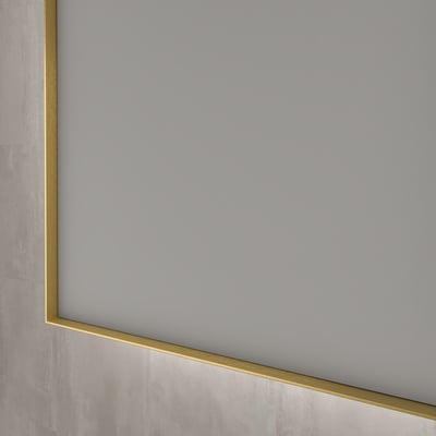 Sanibell INK SP32 spejl, 80x80cm, med en slank, børstet mat guld aluramme, der viser en detalje af kanten mod en grå væg.