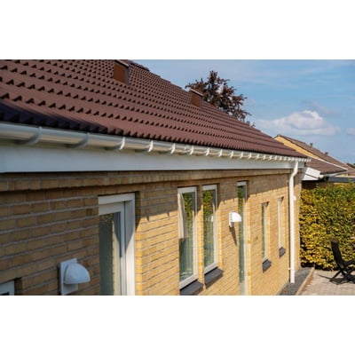 Installation af hvid Plastmo tagrendesystem på gul murstenshus, der viser tagnedløbsrør og tagrende.
