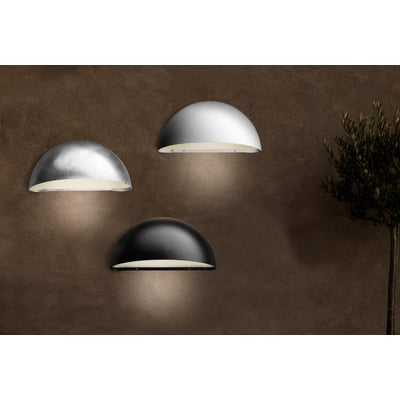 Lumenlight Bolero GII MIDI væglampe i sort, hvid og sølv monteret på mørk, tekstureret væg ved siden af et oliventræ.