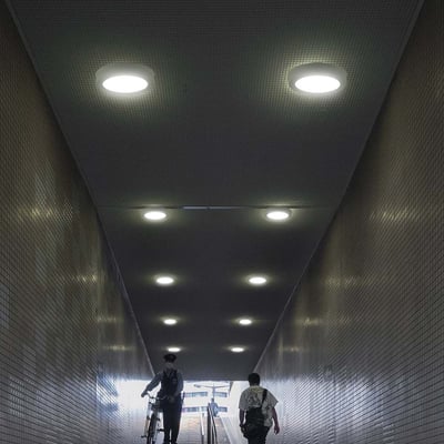 V-TAC rund LED-loftslampe på 12 W med hvid kant lyser i loftet i en lang, flisebelagt passage.