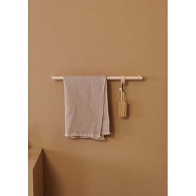 Metallbude Vana håndklædestang i creme med et lyst håndklæde og en børste, vist på en mørkere beige væg.