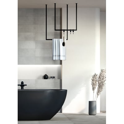 Metallbude Tensi håndklædeholder i sort, firkantet design, vist i et moderne badeværelse med sort badekar og planter.