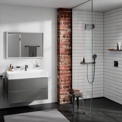 Moderne badeværelse med Hansgrohe håndbruserslange i sort monteret på en bruseniche med hvide fliser og en rustik murstensvæg.