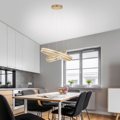 Q-Vito LED pendellampe i messing monteret over et spisebord i et moderne køkkenmiljø, med lyset tændt.