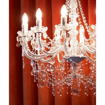 Nærbillede af den 8-armede Nielsen Light Imperial lysekrone med hvidt stel og klare glasprismer mod en orange baggrund.