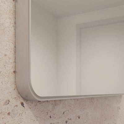 Loevschall Refine spejl med en ramme i børstet aluminium, vist på en rå, stenlignende væg, der fremhæver spejlets moderne design.