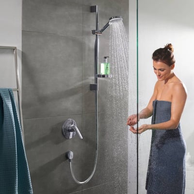 Hansgrohe Crometta Vario Unica brusesæt i krom viser brusehoved med vand, en bruseslange og en kvinde i et brusekabine.