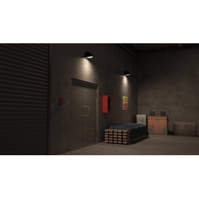 Sort Ansell Lighting WOLF væglampe med sensor, monteret på betonvæg ved dør, med asymmetrisk lysfordeling.