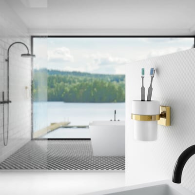 Smedbo house vægmonteret tandglas i hvid porcelæn med poleret messingholder, monteret på væg i badeværelse med udsigt over vand og skov.