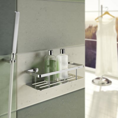 Smedbo Sideline brusekurv i poleret krom med to flasker shampoo, vist på et moderne badeværelsesvæg.