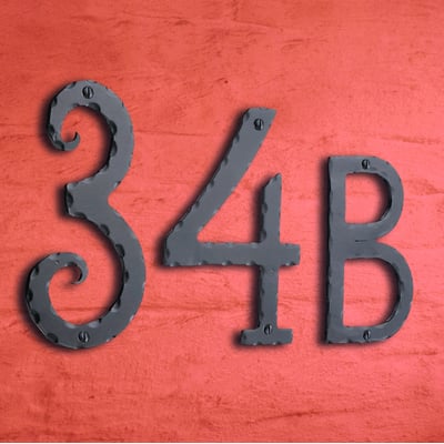 Smedbo husnummer 34B i sort smedejern, monteret på en tekstureret, orangerød facade, der viser nummerets klassiske design og mørke finish.