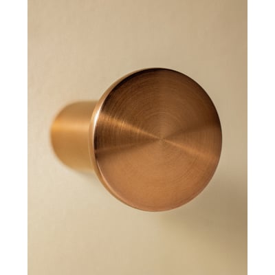 Top view af Cosmic Hook i børstet kobber, med synlig børstet finish og en skygge på den beige væg.