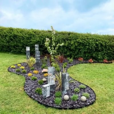 ECCO Products Core Edge kantskinne skaber en flot kant omkring et blomsterbed med barkflis og dekorationer i en have.