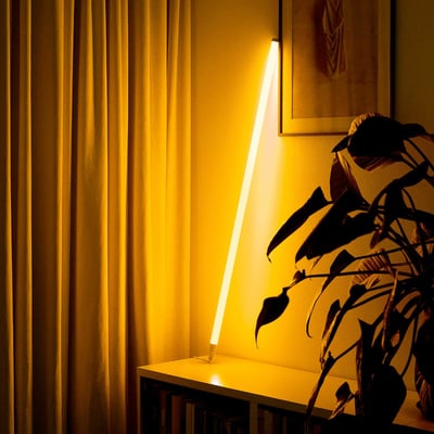 LEDlife Neon Tube LED, 120 cm, gul, lyser skråt op ad et skab ved gardiner og en plante.