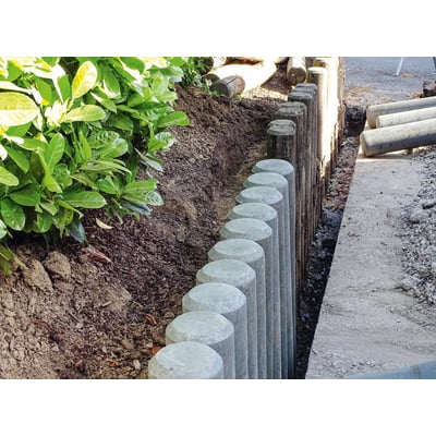 Hanit palisader i genbrugsplast med 10 cm diameter og 60 cm længde, monteret langs et havebed med planter og jord.