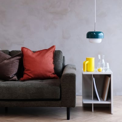 Dyberg Larsen HAIPOT pendel i mørkegrøn og hvid, hængende over et sidebord ved siden af en grå sofa, i en moderne stueindretning.