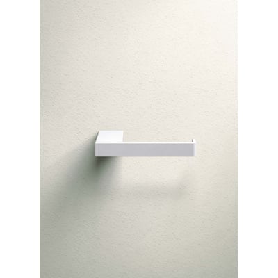 Metallbude Tuali toiletrulleholder i hvid metal, monteret på en lys væg med let tekstur.