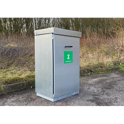 M Stabil 100 liters skraldespand i metal med topindkast og grønt "Madaffald"-mærkat, opstillet udendørs ved et buskads.