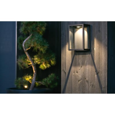 SG Armaturen Fagernes Mini væglampe i sort aluminium med 2700K lys, monteret på trævæg og lyser indirekte.