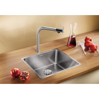 Blanco Andano 450-IF/N UXI køkkenvask i rustfrit stål på en træbordplade med et højt armatur, granatæbler og en karaffel med rød væske.