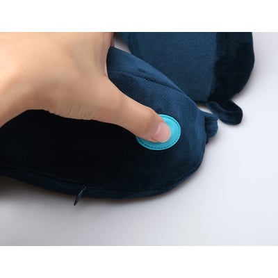 Fingre trykker på den blå knap på Travel Blue Massage Tranquility nakkepuden i mørkeblå velour.