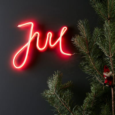 Rød Markslöjd New York Deco Jul Ledtube monteret på mørk væg ved siden af en grankvist med en lille nisse.