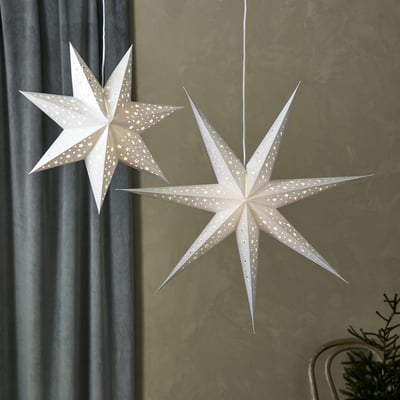 To Markslöjd blanke pendel stjerner i sølv, 75 cm, hængende indendørs i et rum med gardiner og en gren, der skaber julestemning.
