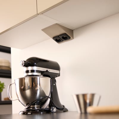 Loevschall dobbelt stikkontakt i ståltrekant design monteret under et køkkenskab med en køkkenmaskine i forgrunden.