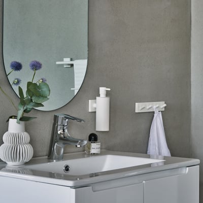 Smedbo House firekrog i mat hvid med fire knage, monteret på en grå væg over et hvidt vaskebord med armatur og vase.