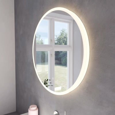 Atlas Loevschall spejl, Ø60 cm, rundt med dæmpbart backlight, monteret på grå væg ved et vindue.