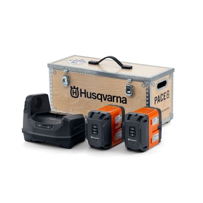 Husqvarna PACE power kit med B750X batteri og C1800X oplader, præsenteret foran en trækasse med Husqvarna logo.