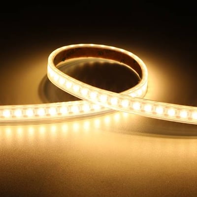 Fleksibelt K-Cell LED bånd fra Ansell Lighting, med varmt hvidt lys, bøjet i en cirkel på en mørk reflekterende overflade.