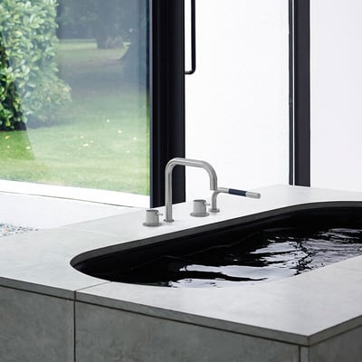 Vola SC10-16 krom vandhane med 2-grebs betjening monteret i karkanten på et moderne badeværelse med udsigt til grønne områder.