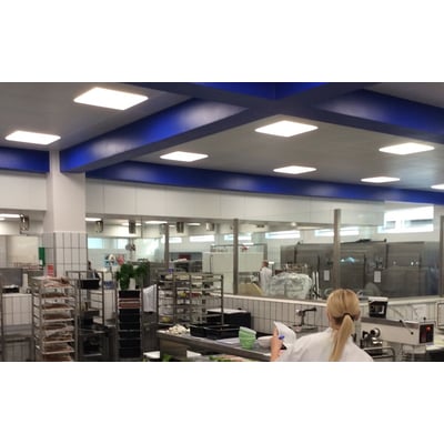 SG Armaturen Sense Eco LED-panel på 600x600 mm monteret i loftet i et industrielt køkkenmiljø med blå bjælker.