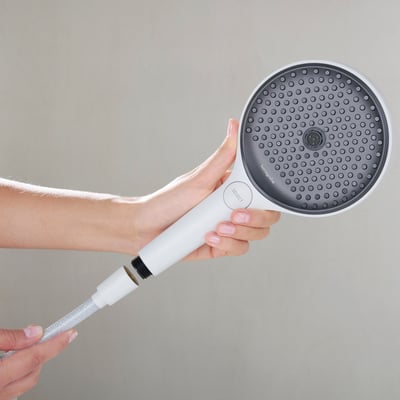 Person holder en Hansgrohe håndbruser med hvidt greb, mens den hvide bruserslange med tekstilflet er tilsluttet.