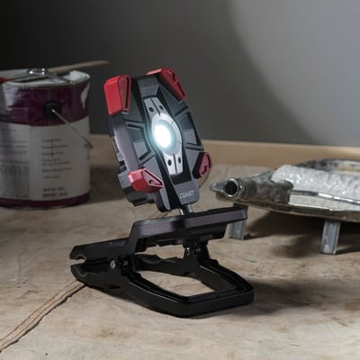 Coast CL40R LED arbejdslampe med clip-fod, oplyser et arbejdsområde med maling og værktøj i baggrunden.