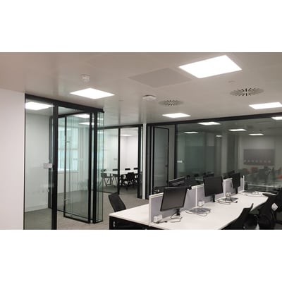 SG Armaturen Sense Pro X 600x600mm panel med 4000K hvidt lys, installeret i et moderne kontor med glasvægge og skriveborde.