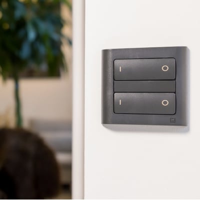 Koksgrå ZigBee tryk til lysstyring monteret på hvid væg, med to vippekontakter til On/Off funktion.