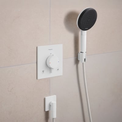 Hansgrohe Raindance Alive S håndbruser i mat hvid med grafitsort brusehoved monteret på en cremefarvet flisevæg.