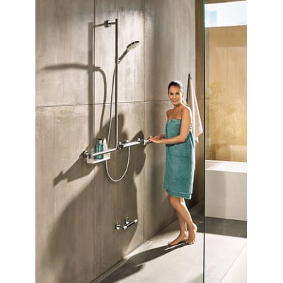 Hansgrohe håndbruserarrangement med 1100 mm stang, 1.6m slange og hylde, vist i et moderne badeværelse med en kvinde iført et håndklæde.