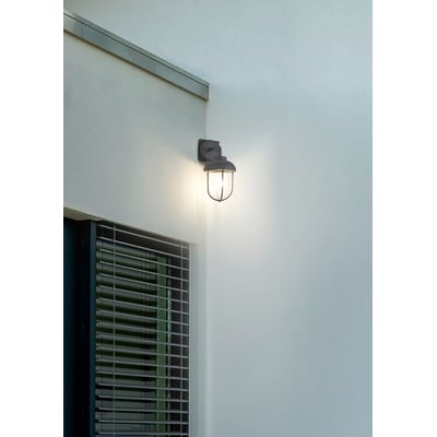 Trio Lighting hjørnefæste med en tændt udendørs væglampe, placeret på et hjørne ved et vindue med persienner.