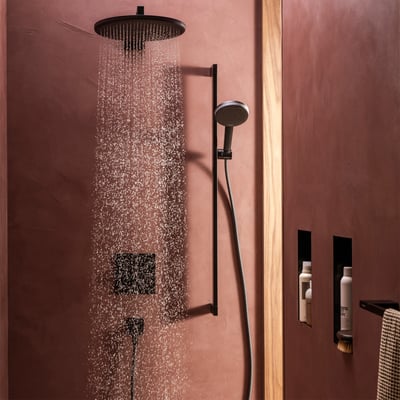 Hansgrohe Raindance Alive S håndbruser i mat sort, vist i brug med brusehoved, der sender PowderRain stråler mod en rustik væg.